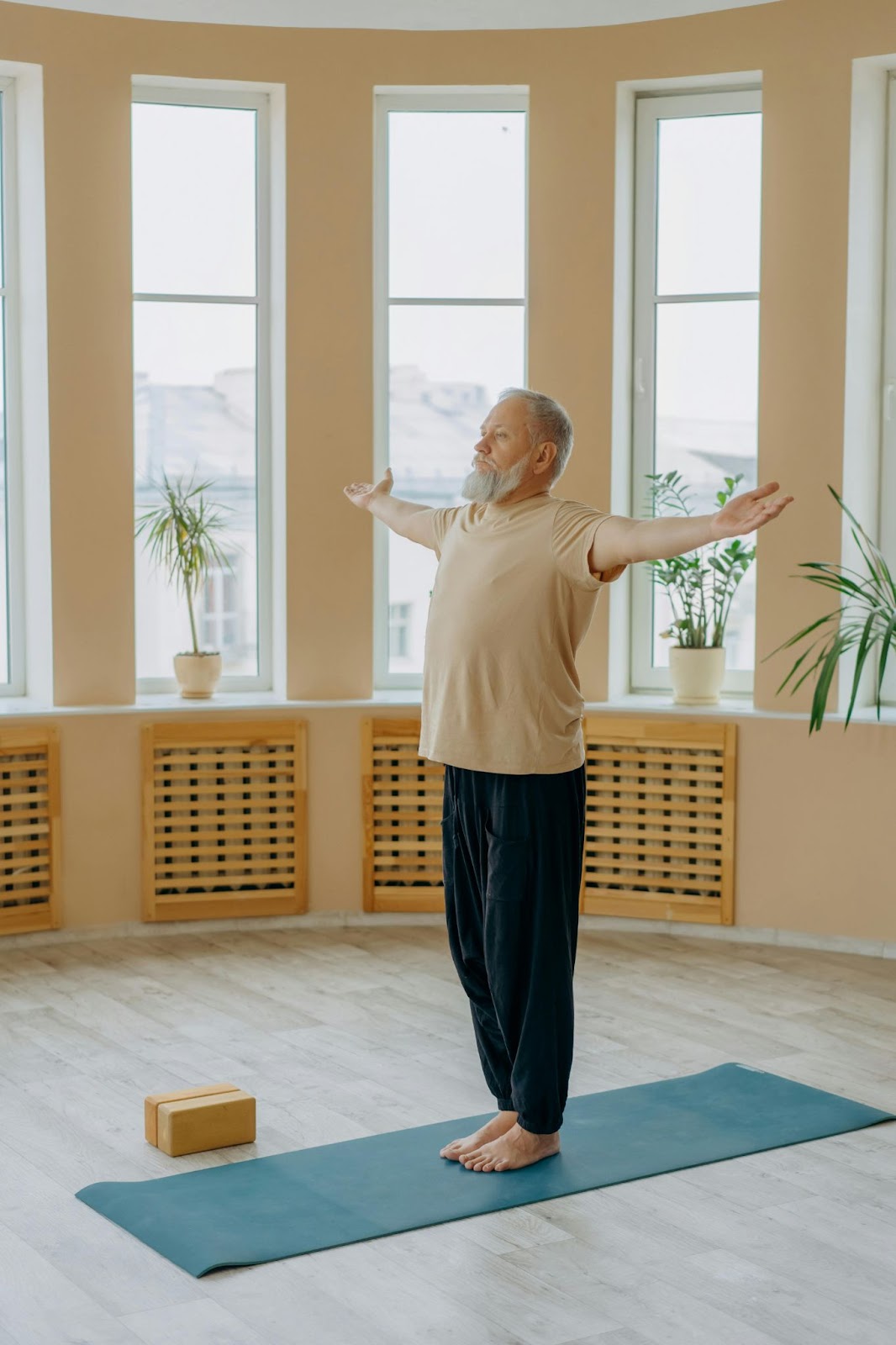 A man stands on a yoga mat and raises his arms.