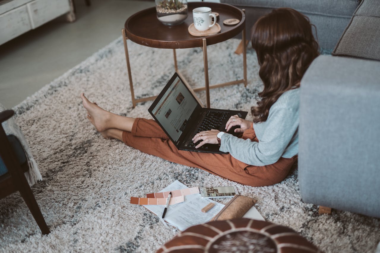 A person working on a laptop at home, surrounded by notes and coffee