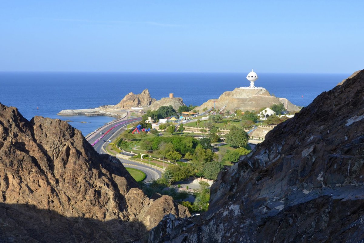 Scenic view of Riyam Park and the iconic incense burner monument in Muscat, Oman, with winding coastal roads and the blue waters of the Gulf of Oman in the background.