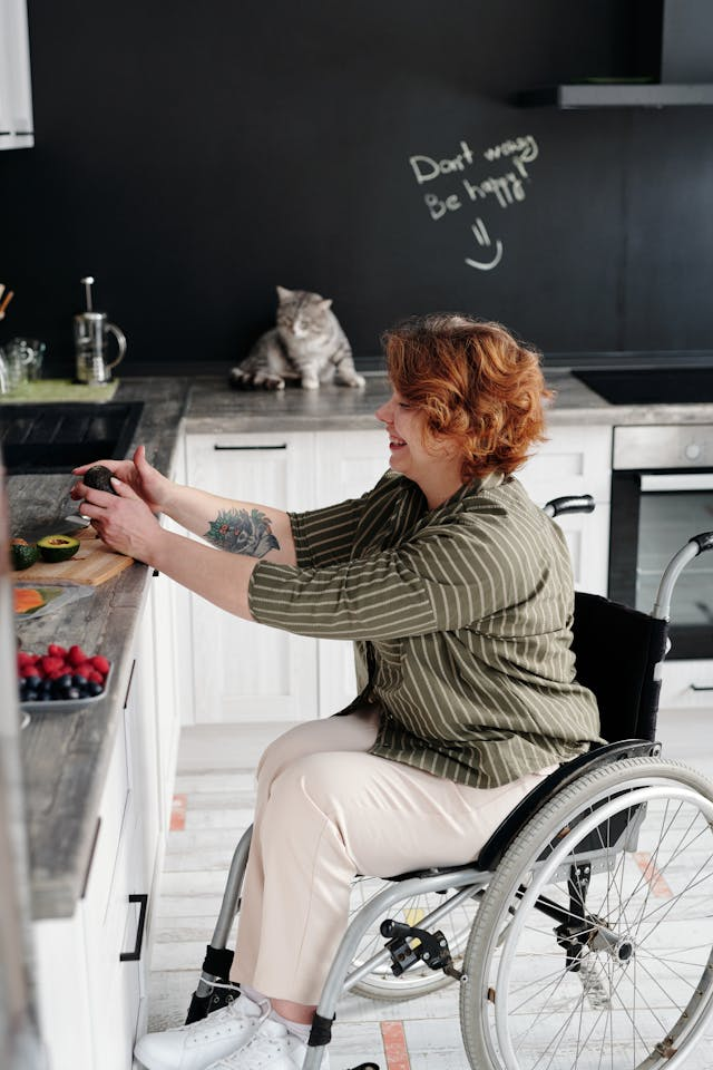 A woman in a wheelchair with a tattoo on her arm is preparing food in a modern kitchen designed with ergonomic solutions.