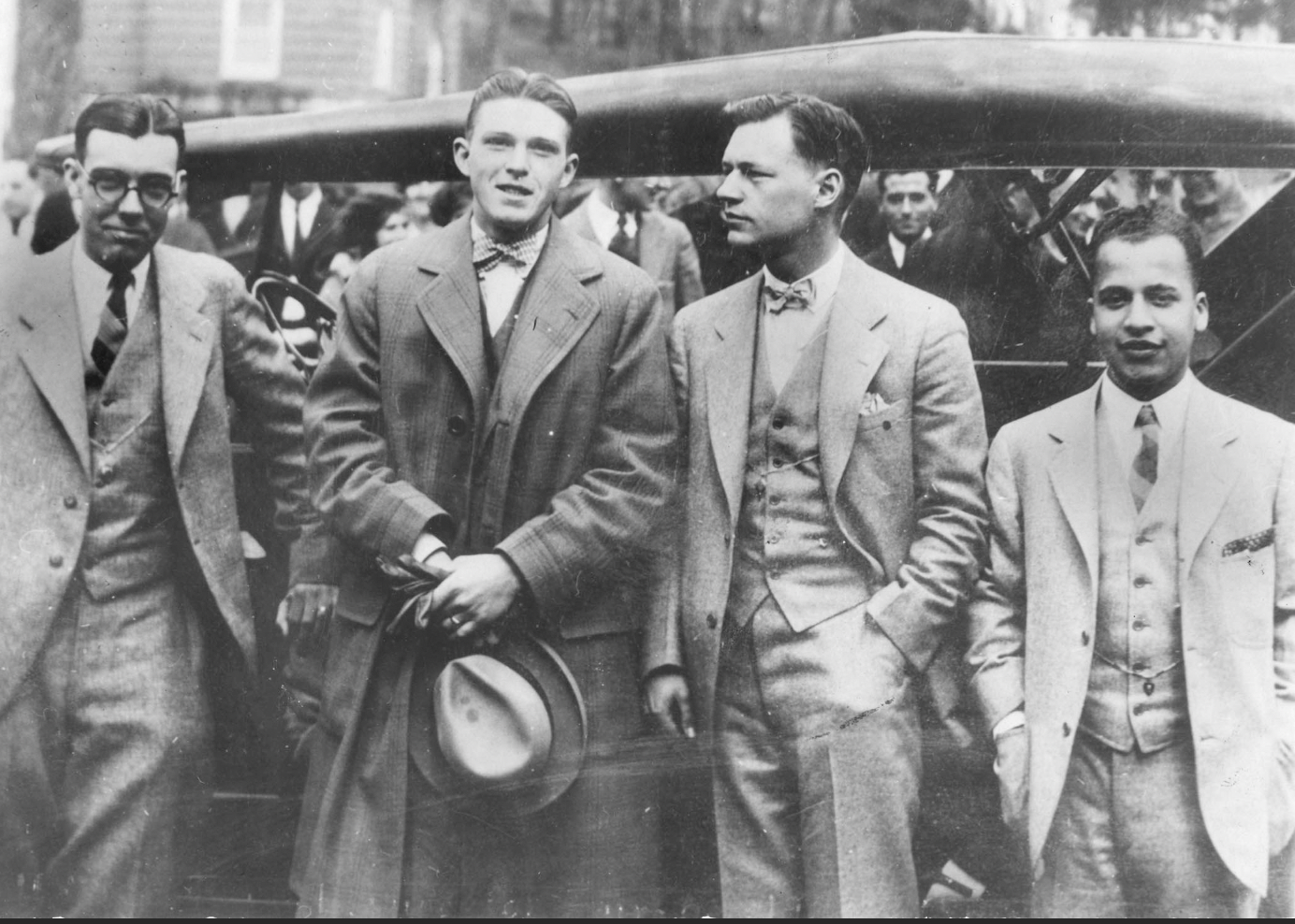 four early 20th century debaters and their coach in suits in front of a car