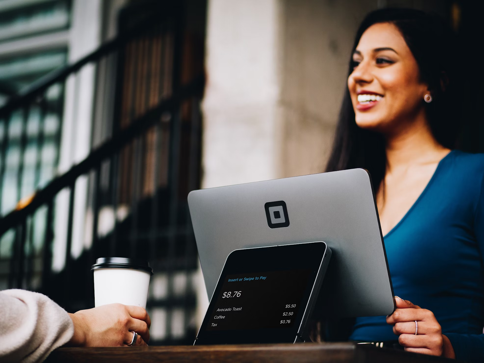 Charming stylish young female assistant working on laptop smiling, hand holding coffee mug, sitting at her workplace