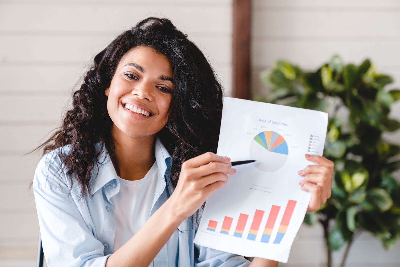 Woman holding a piece of paper and pointing at a pie chart with a pen. 