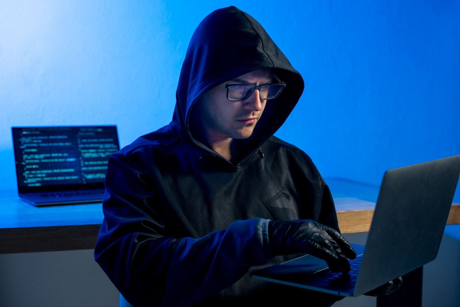 Hacker in dark hoodie typing on a laptop in a dimly lit room