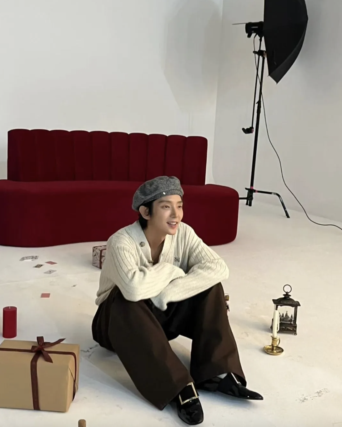 A picture of Lee Joon Gi on a coffee brown trouser and a off-white shirt and a ash colour cap sitting on the ground 