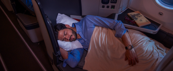 Homem descansando em um assento flatbed na classe executiva da Avianca, com travesseiro e cobertor, mostrando conforto e espaço pessoal em uma cabine de avião premium.