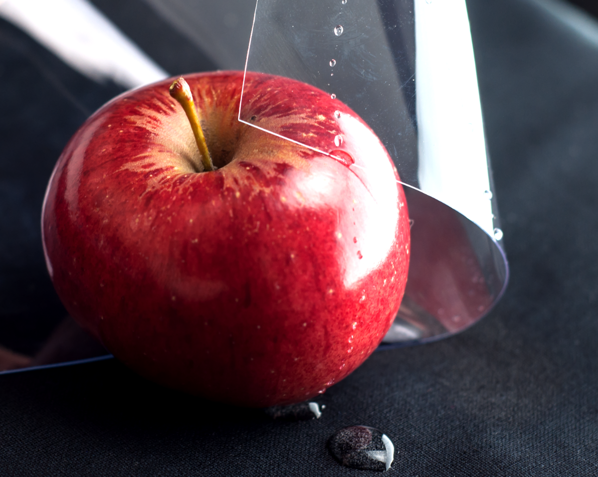 Une feuille brillante et transparente de vinyle PVC recouvrant partiellement une pomme rouge avec des gouttelettes d'eau sur sa surface, démontrant ses propriétés alimentaires sûres.