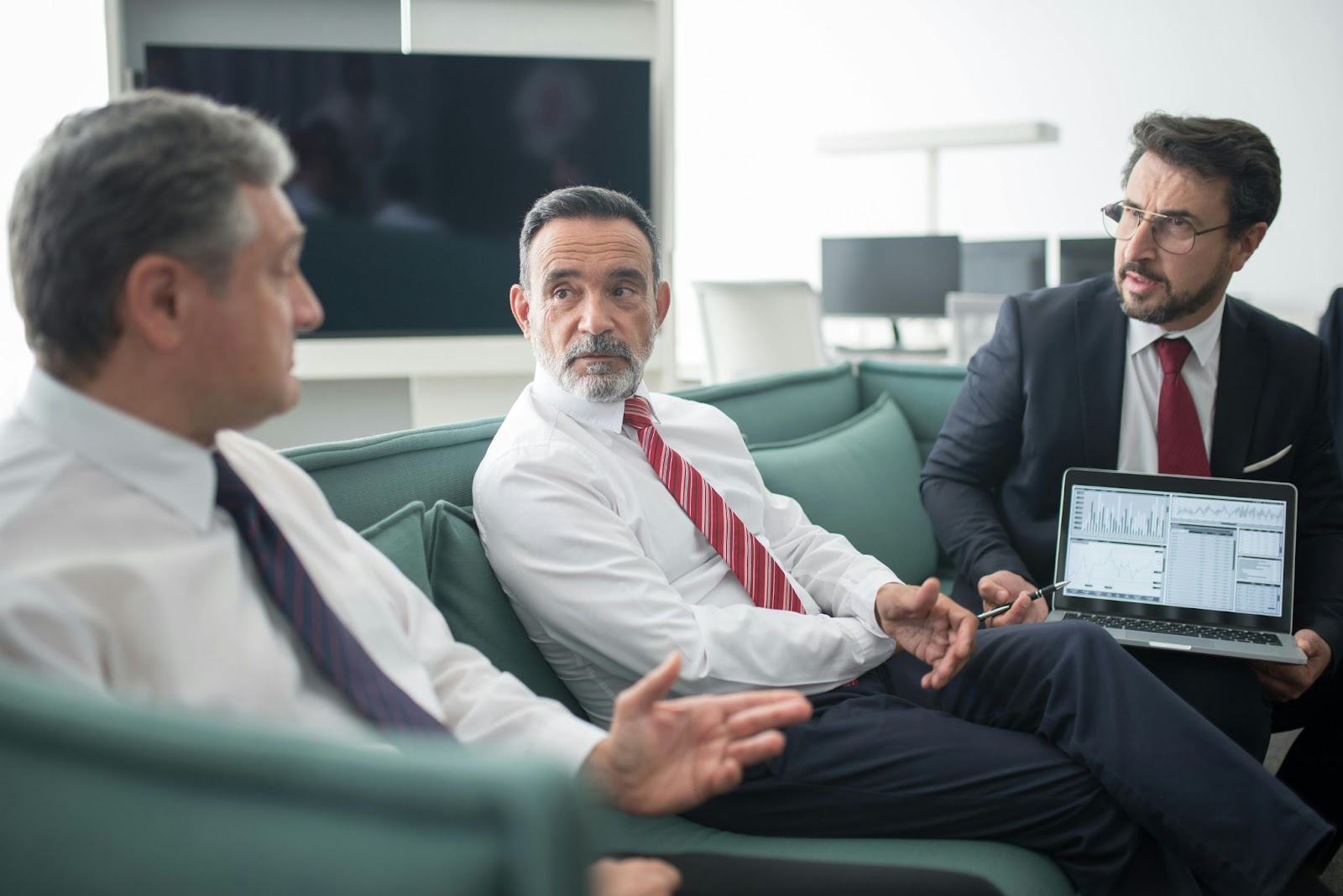 Three businessmen discuss while sitting on a couch in an office.