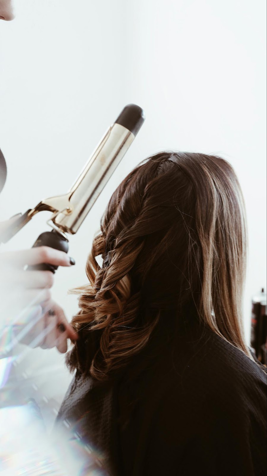 Stylist curling hair with hot iron after clip-in extension placement
