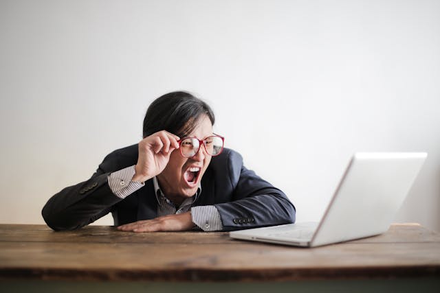 A suited man infront of a laptop shows a shocking reaction of what he saw in his laptop