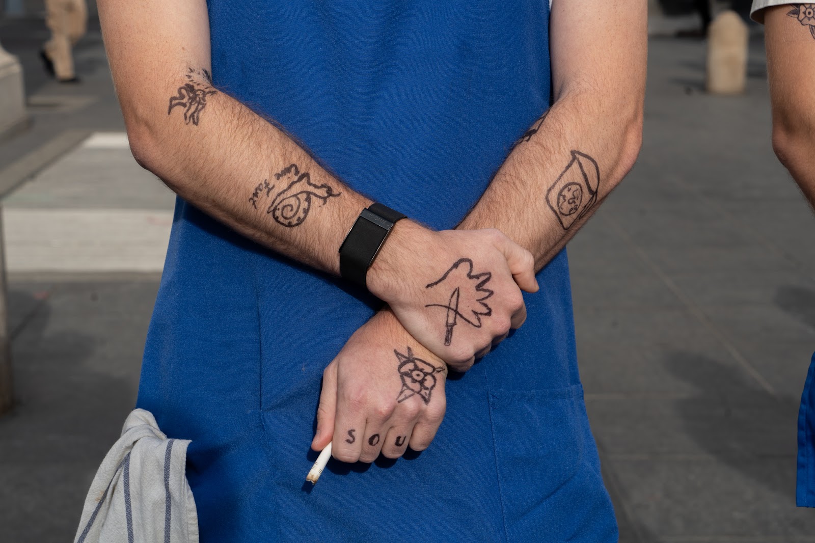 An image of a contestant’s hands, with drawn-on tattoos and a cigarette, resembling Jeremy Allen White’s.
