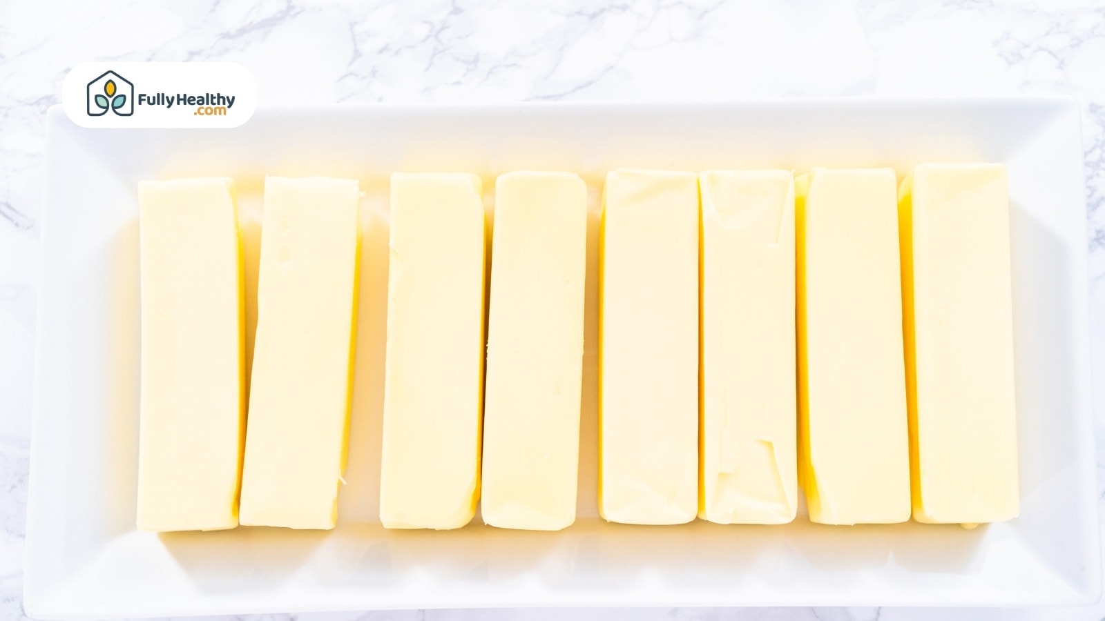 Eight uniform butter sticks arranged on rectangular white plate
