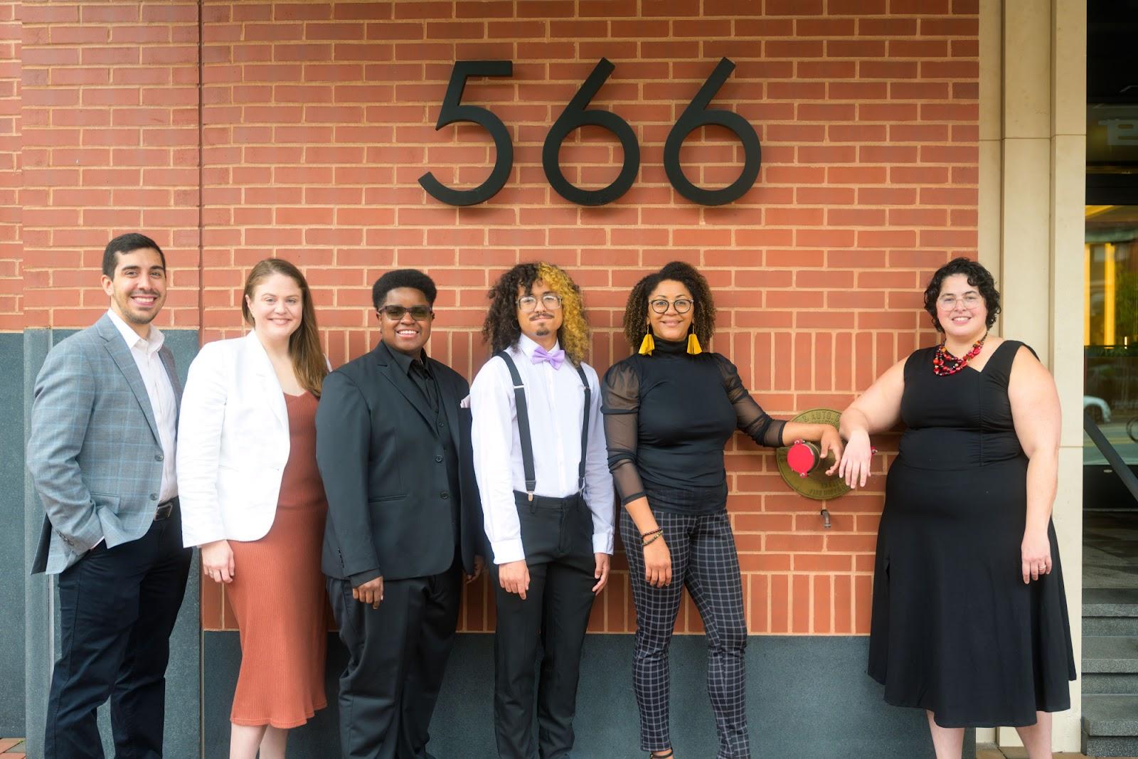 A group of people standing in front of a brick building</p>
<p>Description automatically generated