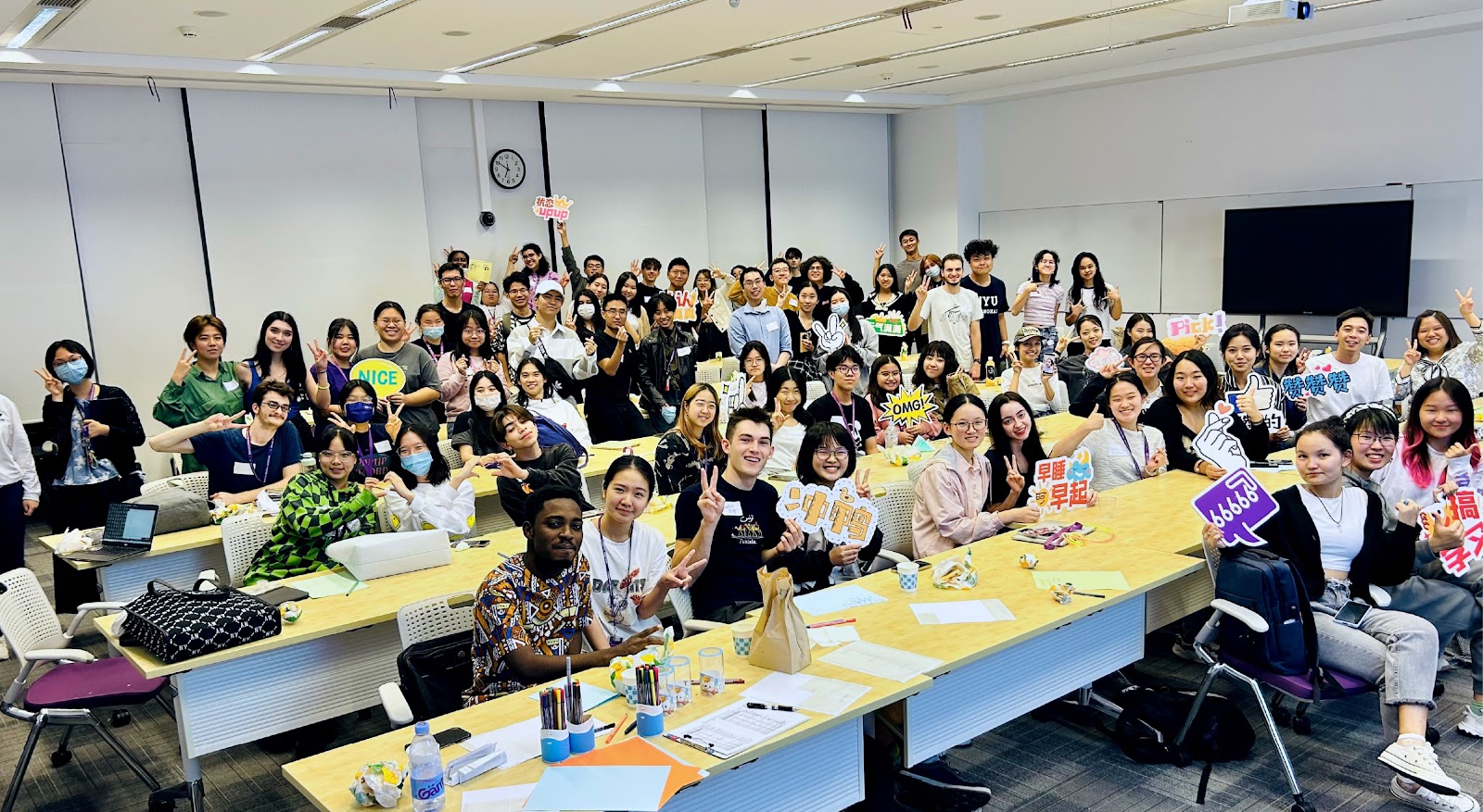 a large group of students sitting behind tables holding signs and smiling at the camera