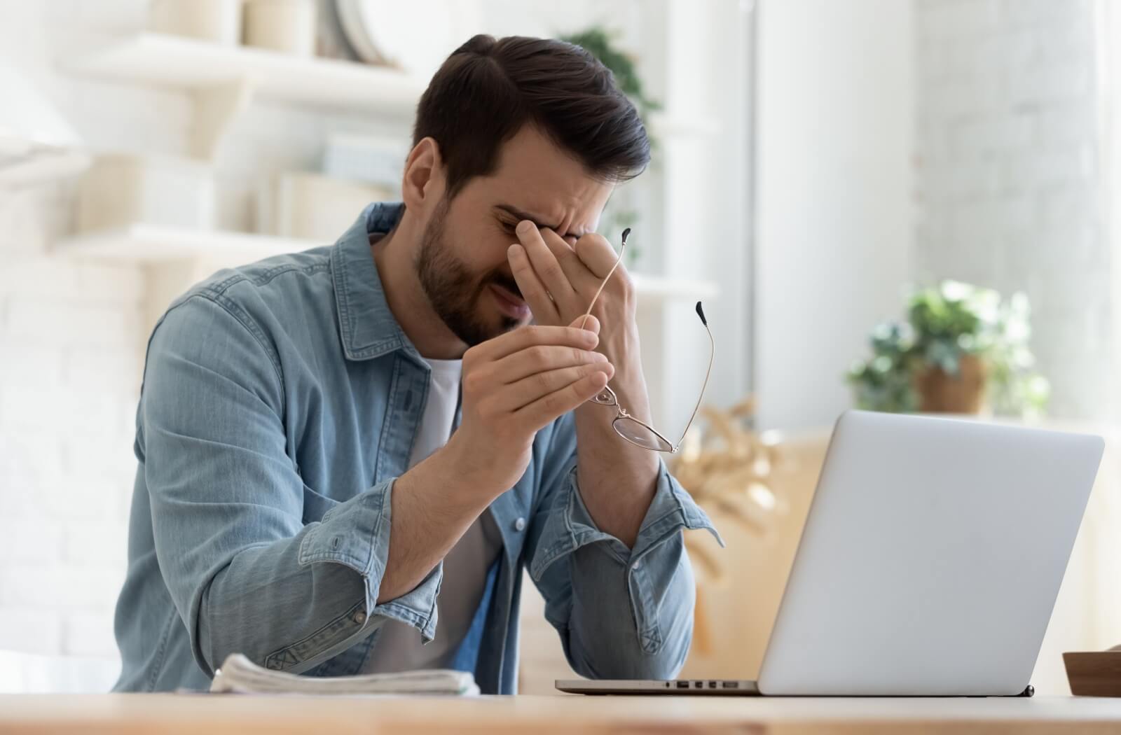 A person working on a laptop stops to rub their eyes due to eye strain.