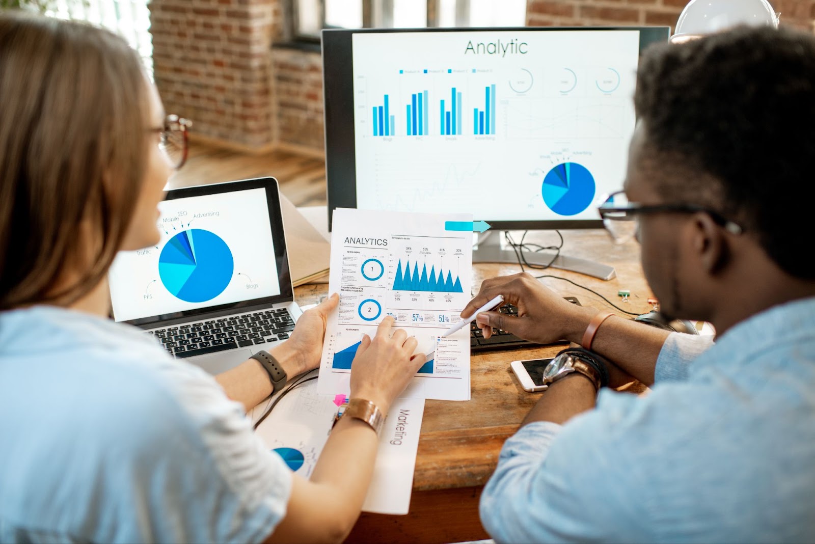 Man and a woman looking at analytics on a piece of paper and a computer. 