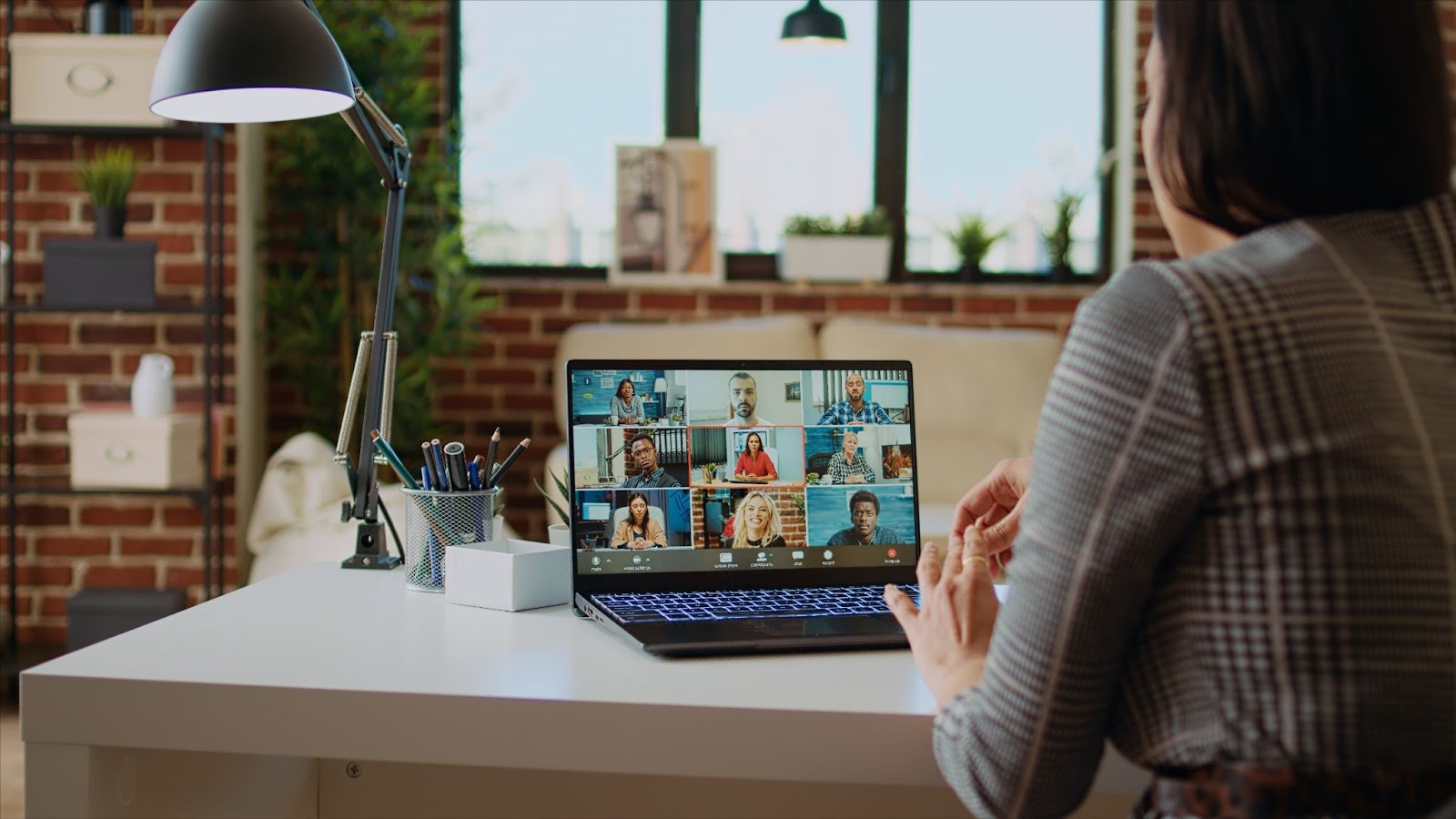 A woman sitting at a desk participating in a virtual video conference with multiple people displayed on her laptop screen.