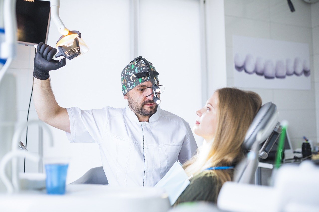 Dentist pulling light down closer to the patient, who is in the dental chair 