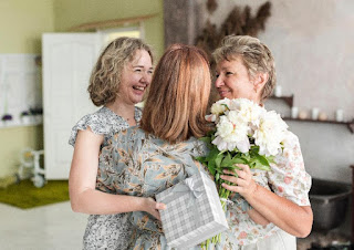 mother-daughter-hugging-their-grand-mother-with-holding-gift-flower-bouquet-home