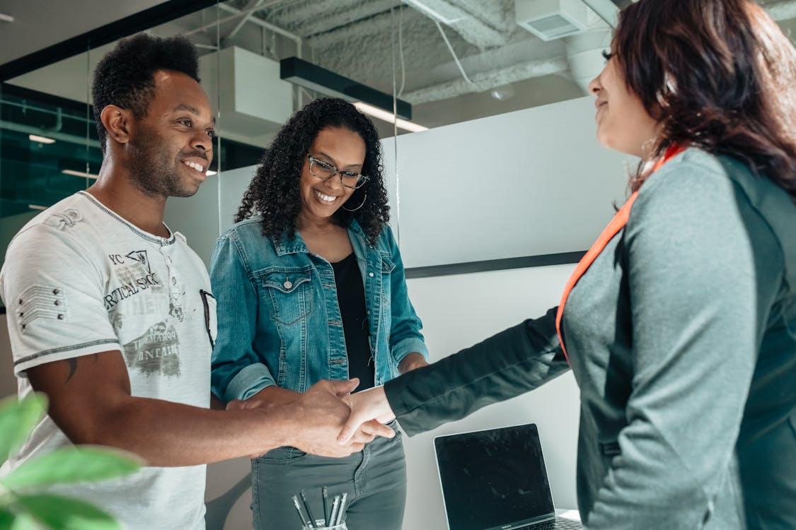 Free Smiling couple shaking hands with advisor in modern office. Stock Photo
