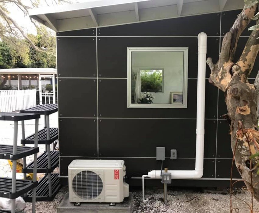 An HVAC unit hooked up to an outdoor space with a tree in the right side of the picture