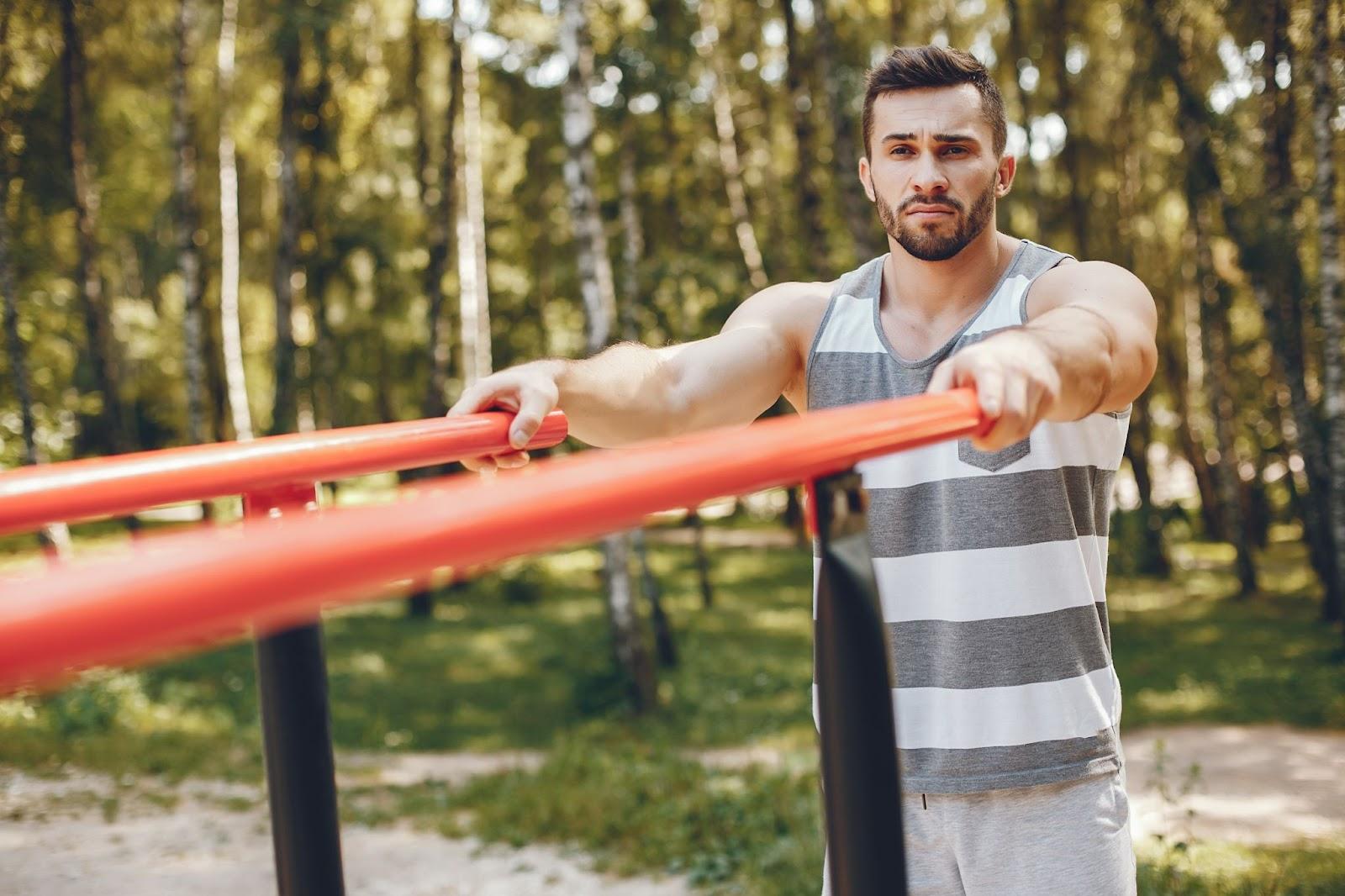 Man focused on outdoor training in Toronto, using park equipment for strength exercises in a sunny, natural setting.