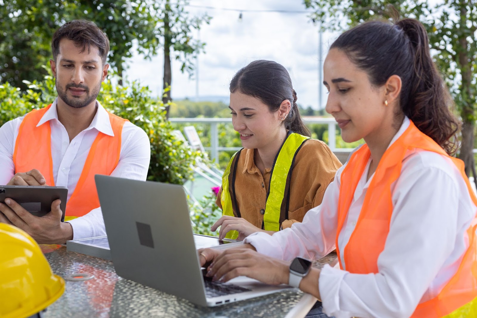 People in vests using laptops outdoors. 