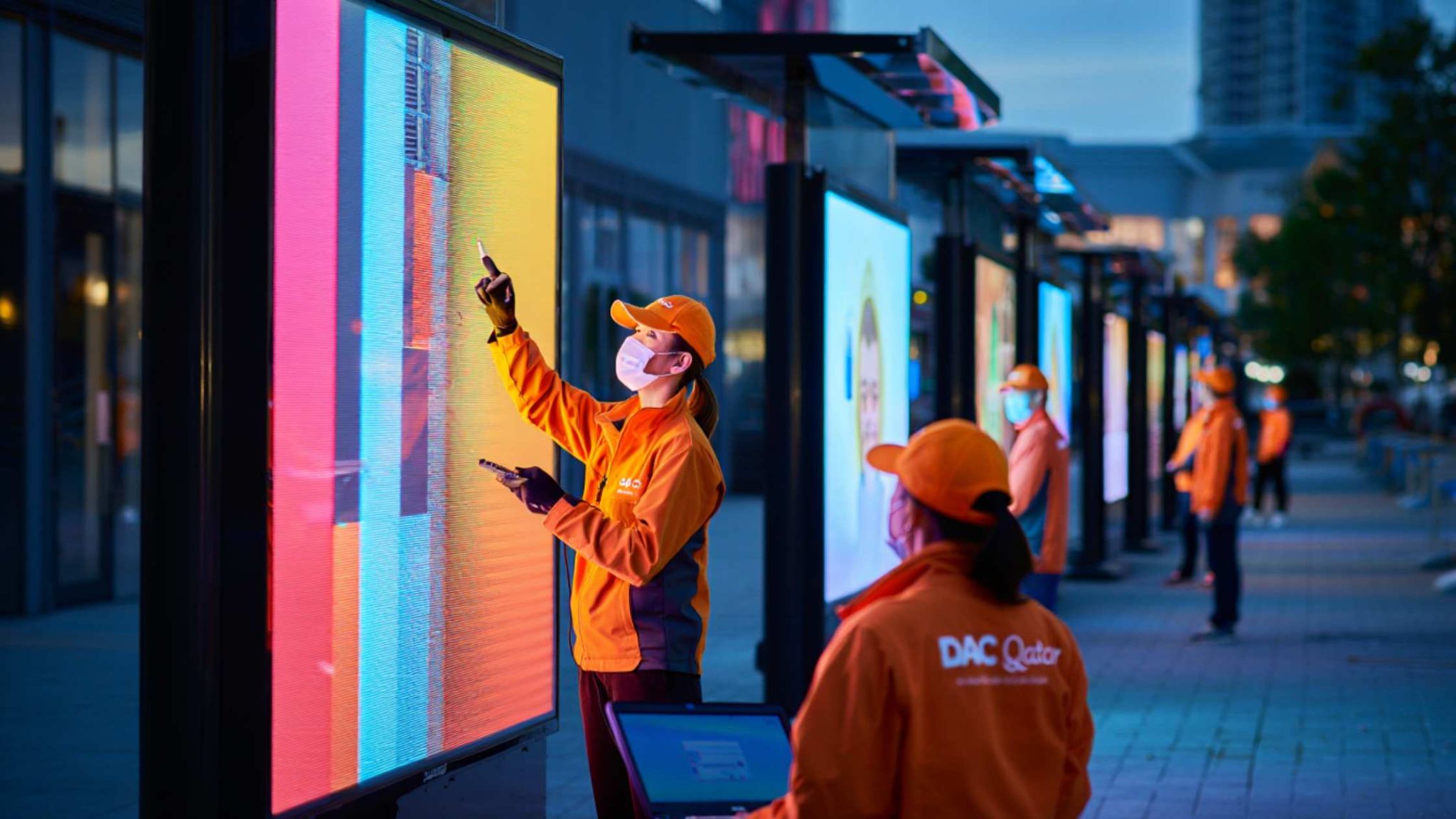 Technicians Calibrating Outdoor Digital Displays – Advertising and Digital Signage Solutions in Doha Technicians working on interactive digital billboards in an urban setting at dusk – Advertising and Digital Signage Solutions in Doha