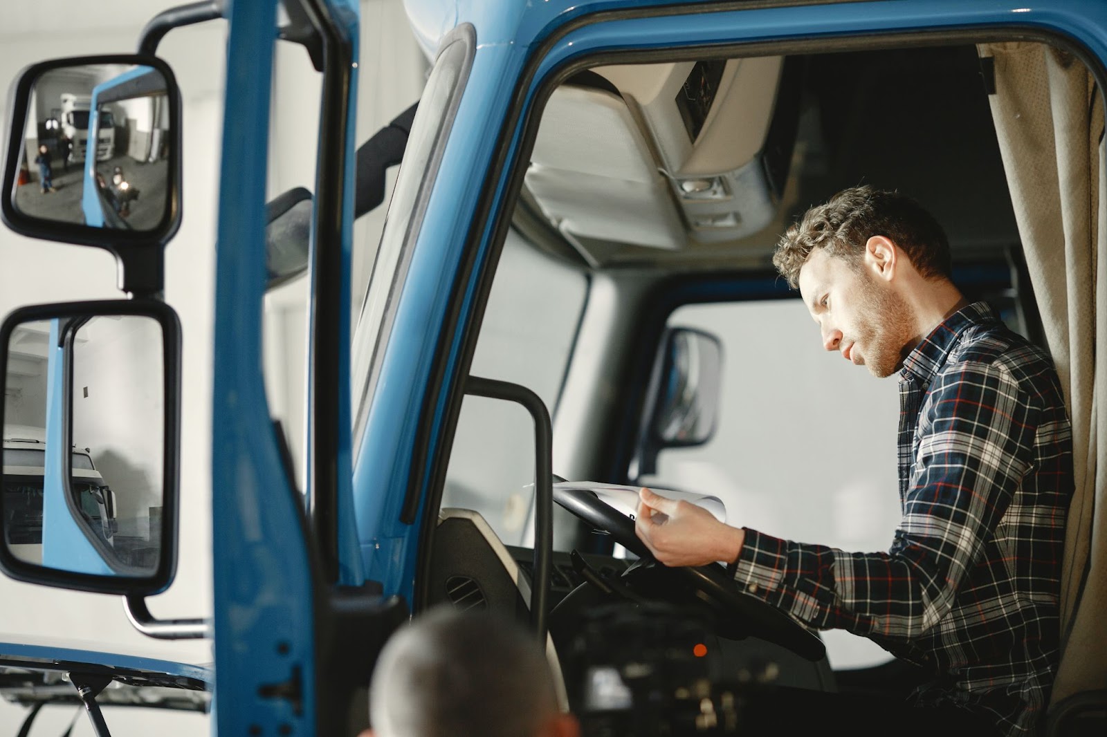 A person staring at a notebook behind the wheel of a fleet semi truck