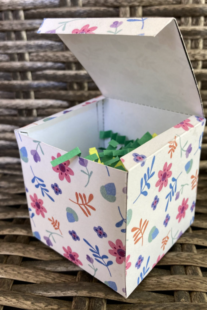 easter egg hunt ideas, white box with flower designs full of green and yellow crinkle paper