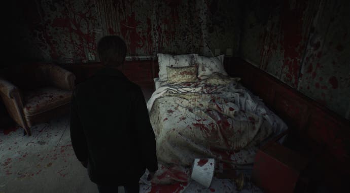 Cuplikan layar dari Silent Hill 2 Remake: James mengamati pemandangan kehancuran total di kamar hotel yang bobrok. Zat merah menutupi setiap permukaan: tempat tidur, dinding, lantai.