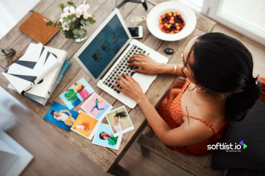 Woman working on a laptop with photos spread around.