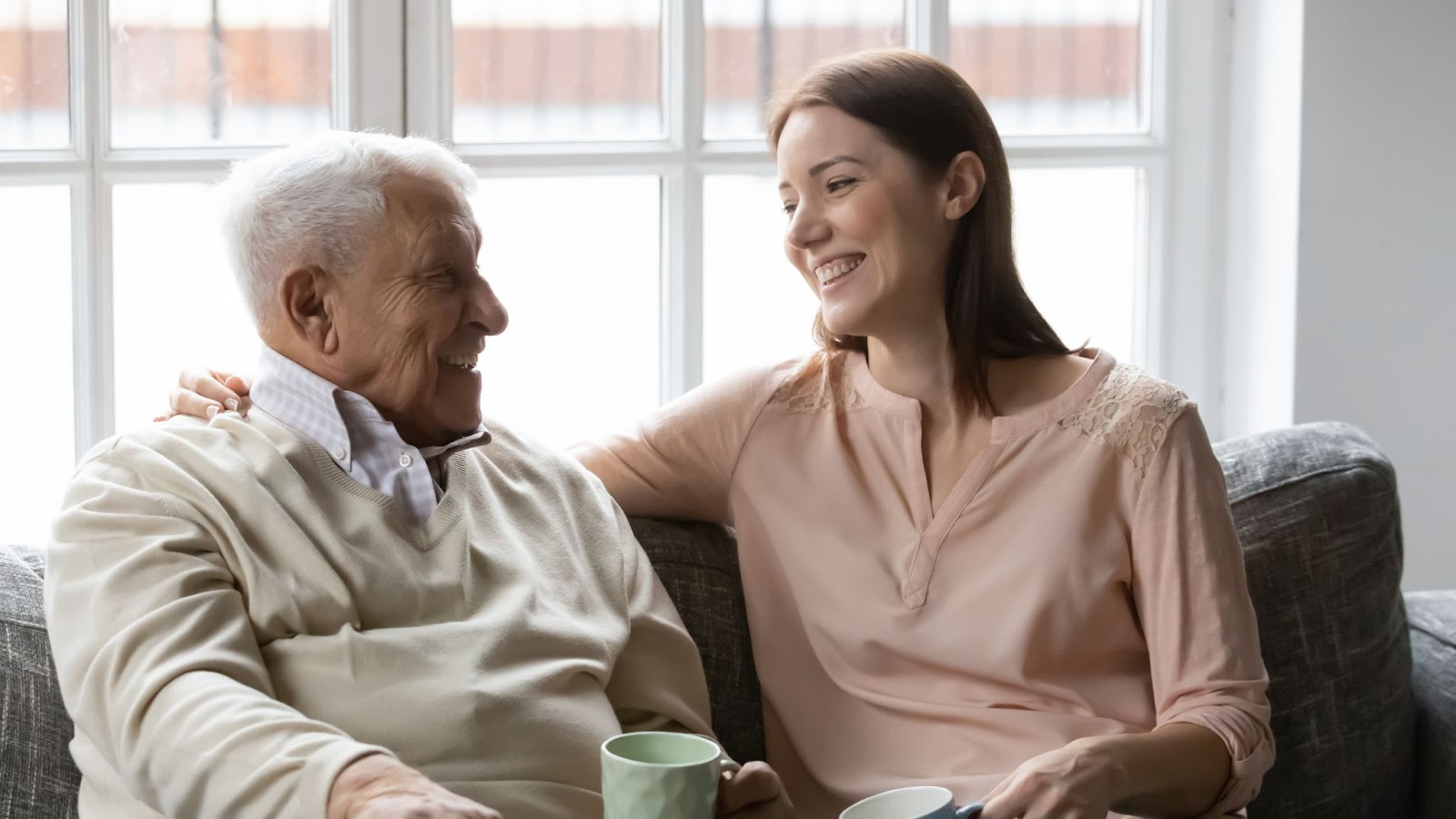 A woman happily chats with her senior father with dementia on a couch.