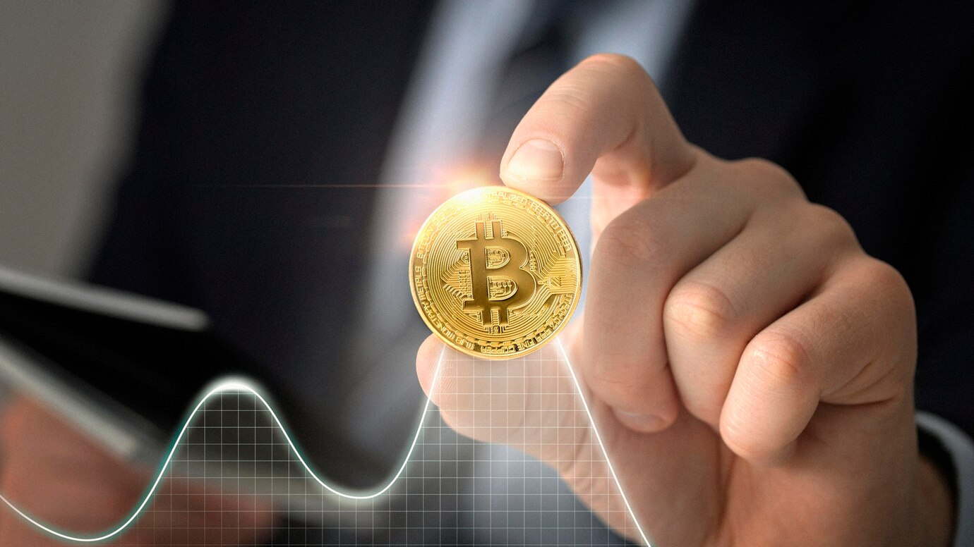 Hand holding Bitcoin coin over a rising graph.
