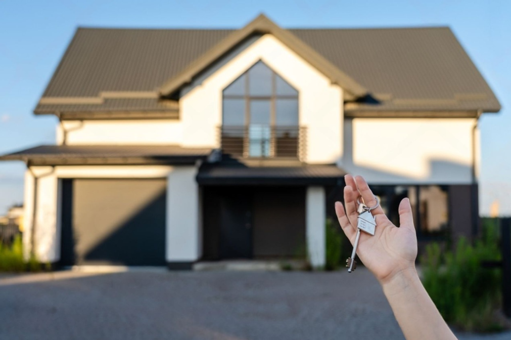 A man is standing in front of a large villa holding a key