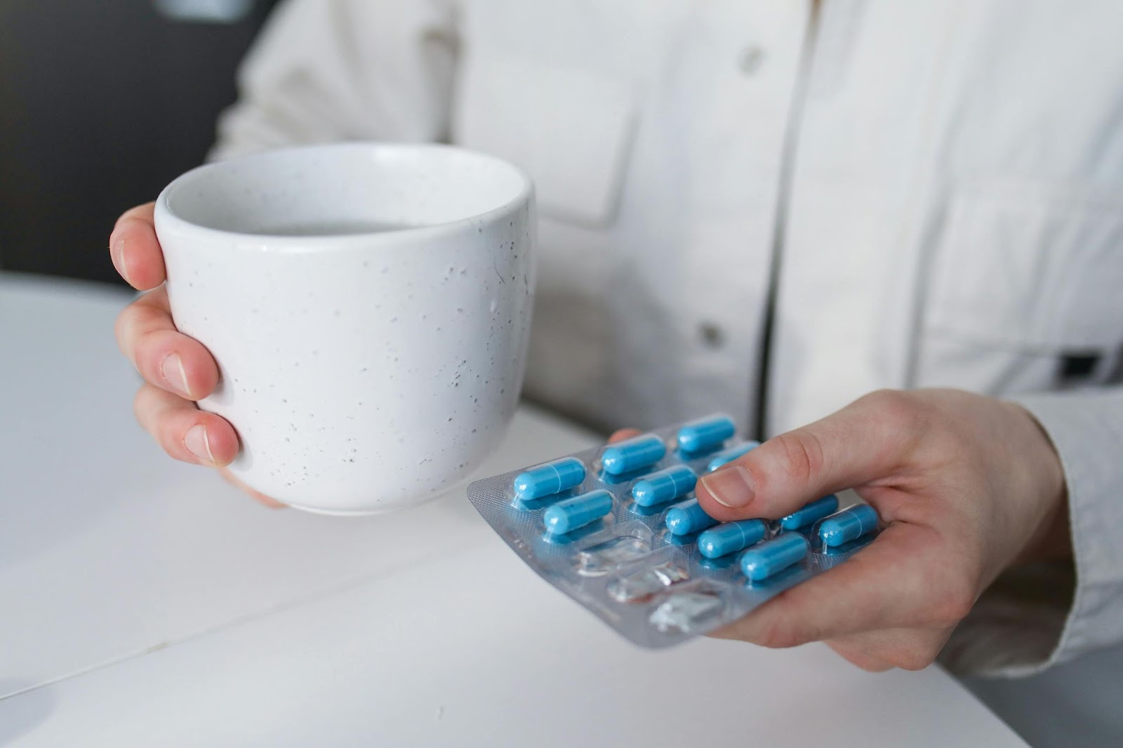 A person holding blue pills and a mug filled with water