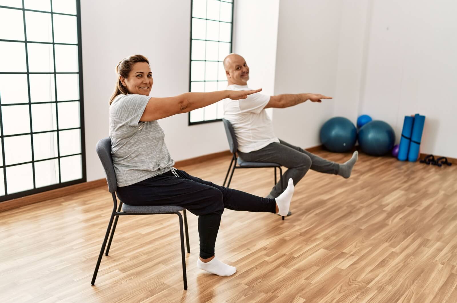 Two smiling older adults doing a core workout on chairs.