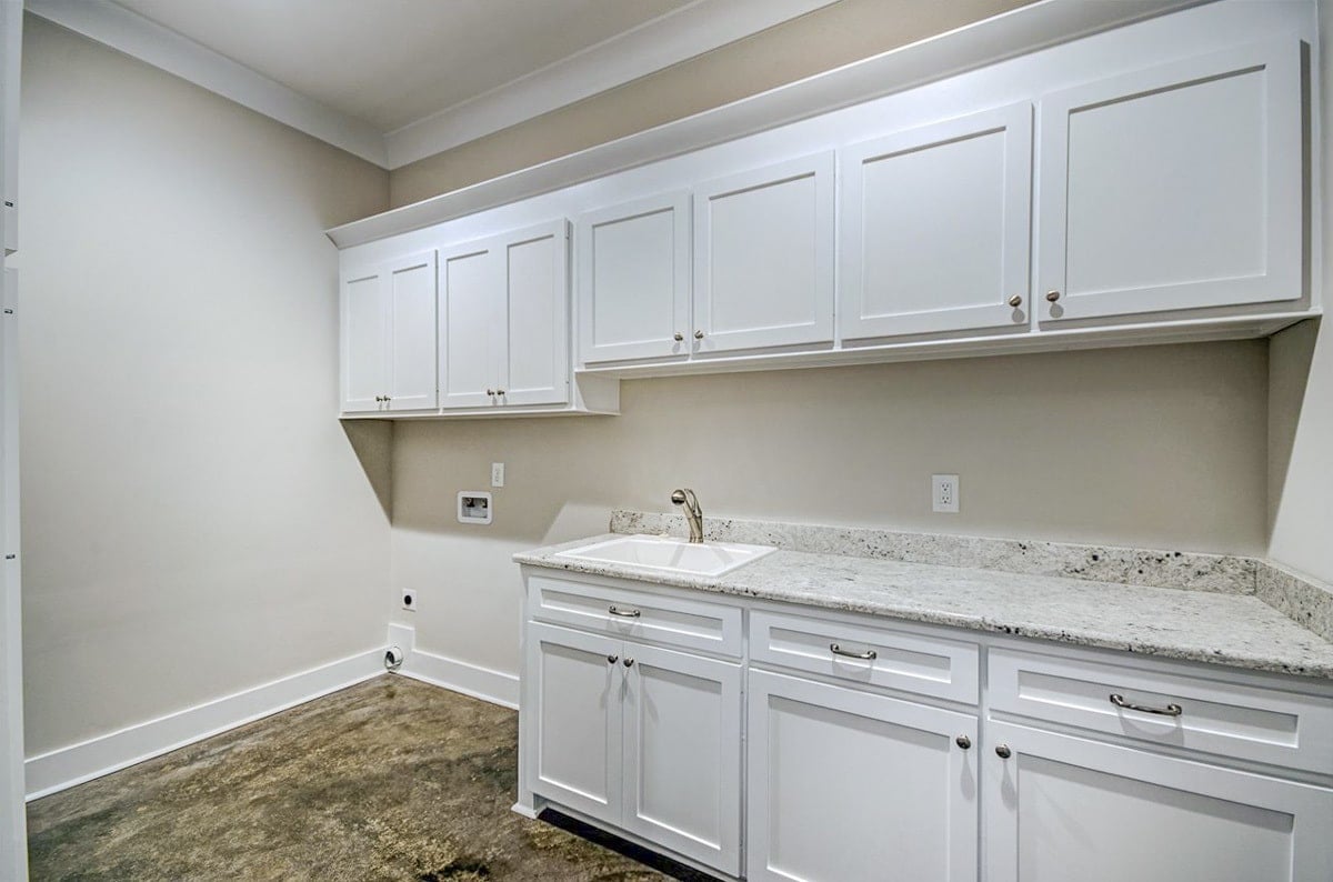 Utility room with white cabinets, granite countertops, and a porcelain sink.