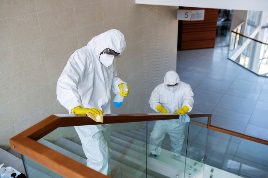 Two exterminators disinfecting a public area in protective suits