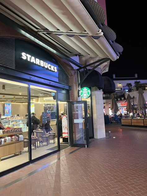 This contains an image of starbucks store with people walking in front and out doors at night on a brick sidewalk