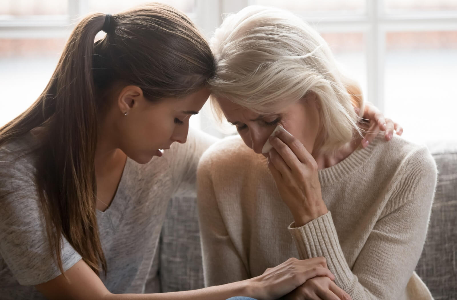 An adult gently consoling their senior parent, who looks unsure and scared while struggling with dementia.