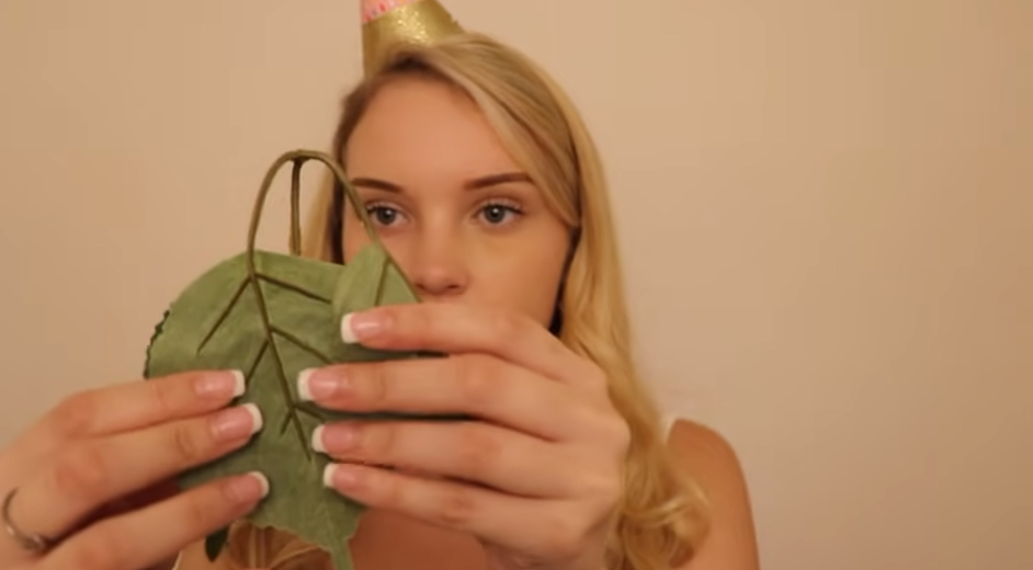 A girl wearing a party hat holds artificial leaves with visible stems and veins, examining them closely.