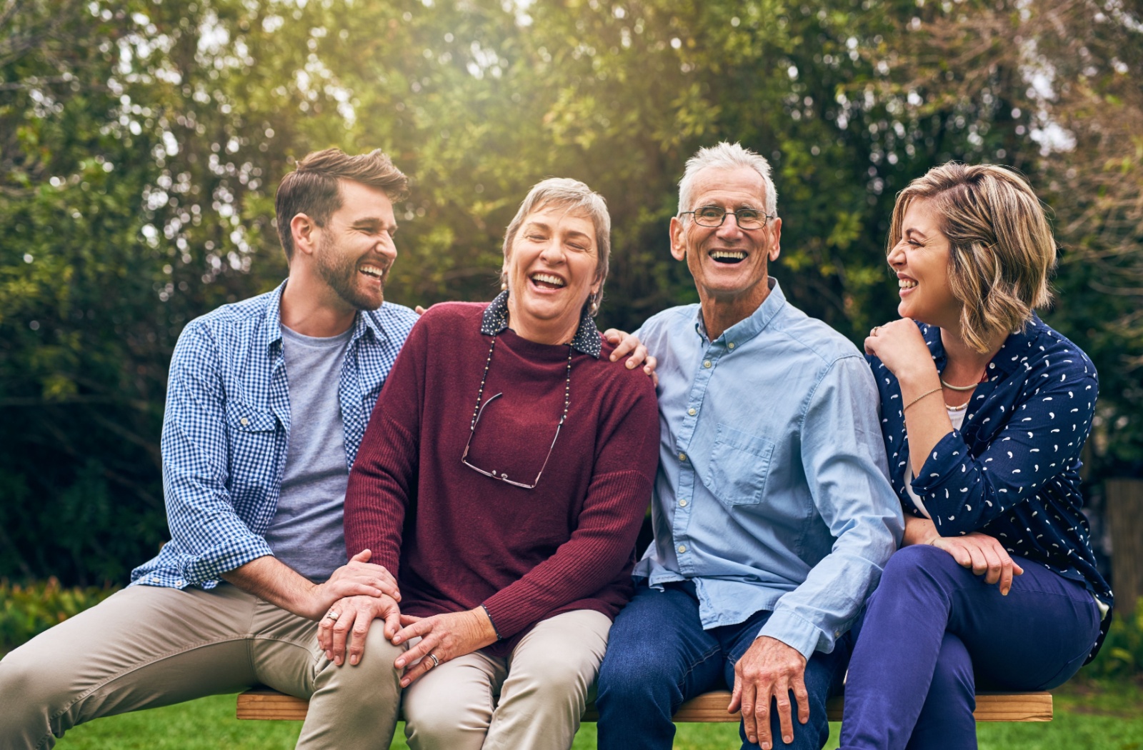 A family of four is smiling, sitting on a park bench outside of a memory care community.