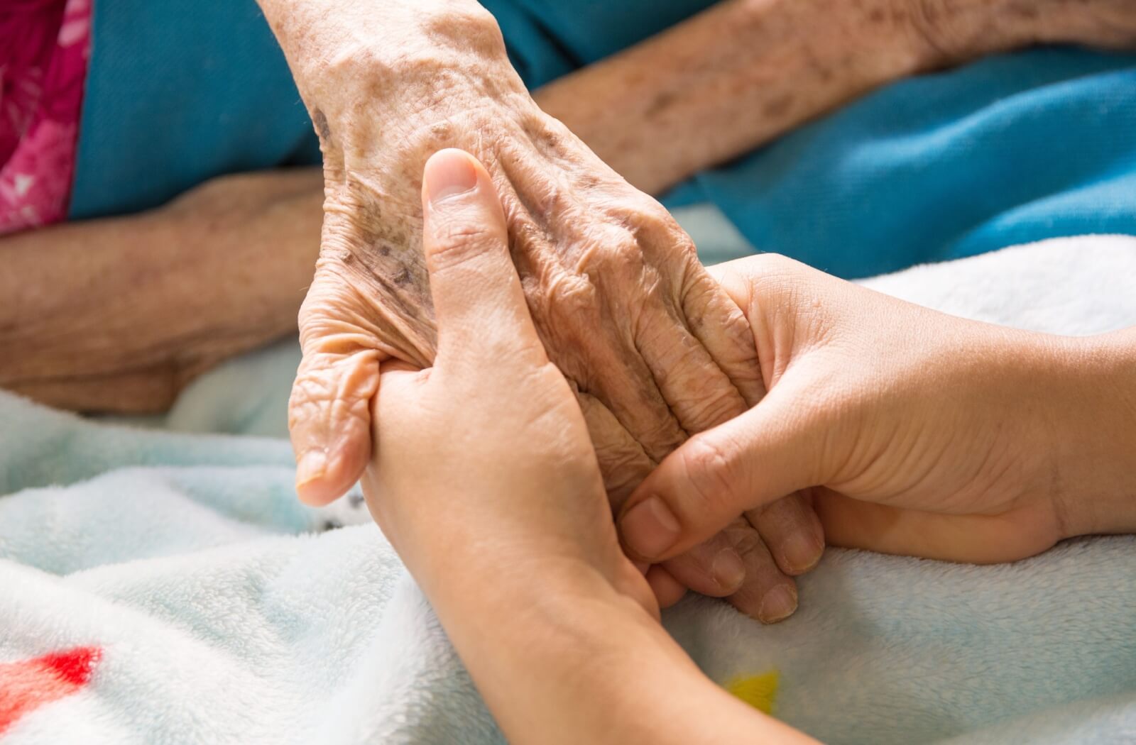 Close-up of an older adult's hands held by a younger caregiver's hands, symbolizing compassion, connection, and supportive dementia care