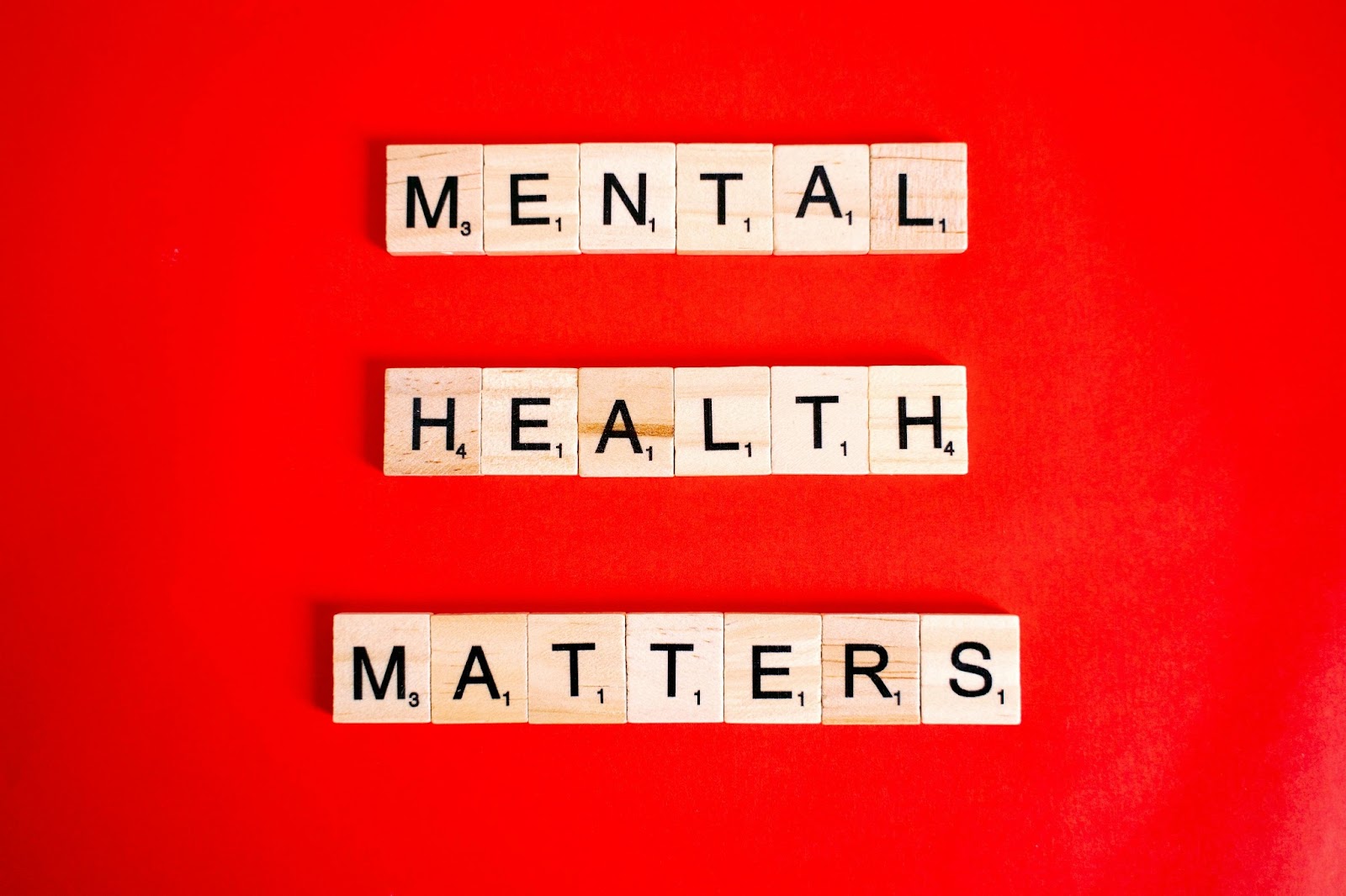 The words 'Mental Health Matters' spelled out with wooden tiles on a bright red background.
