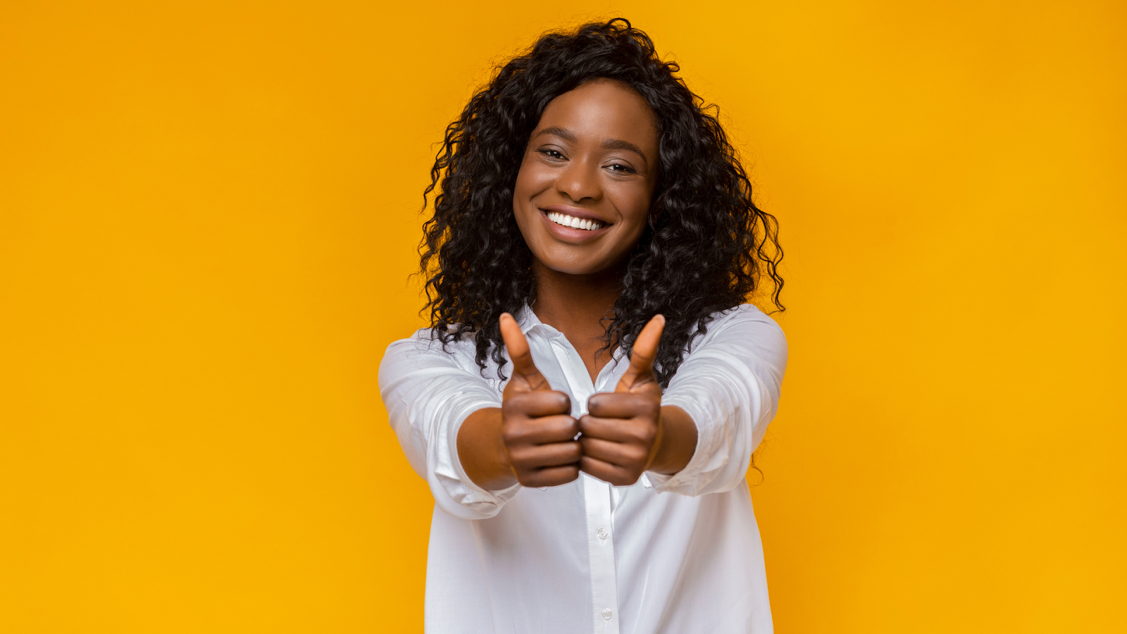 Woman holding her thumbs up, yellow wall // Healthier Baby Today