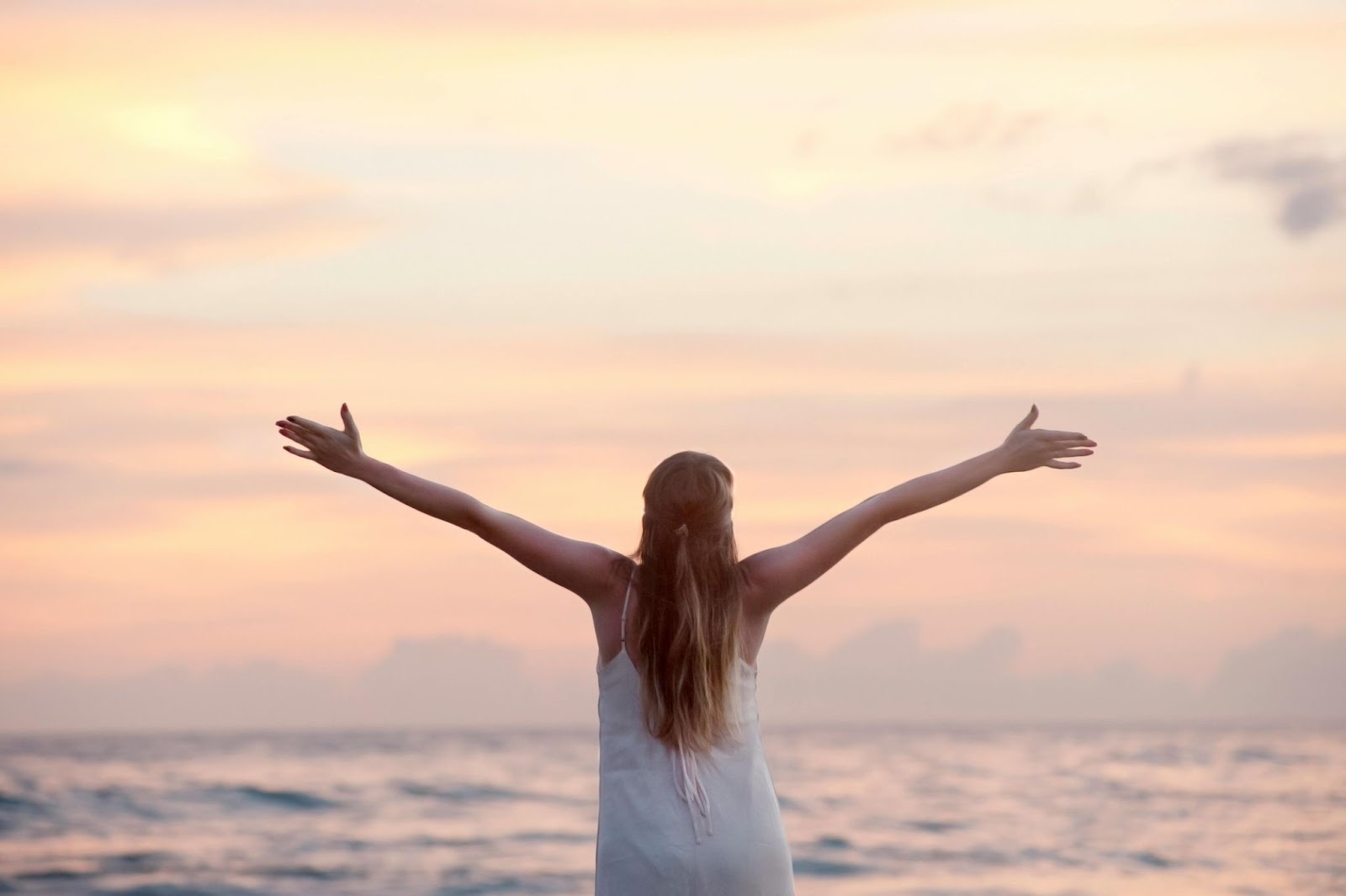 A woman raises her arms on a beach at sunrise.