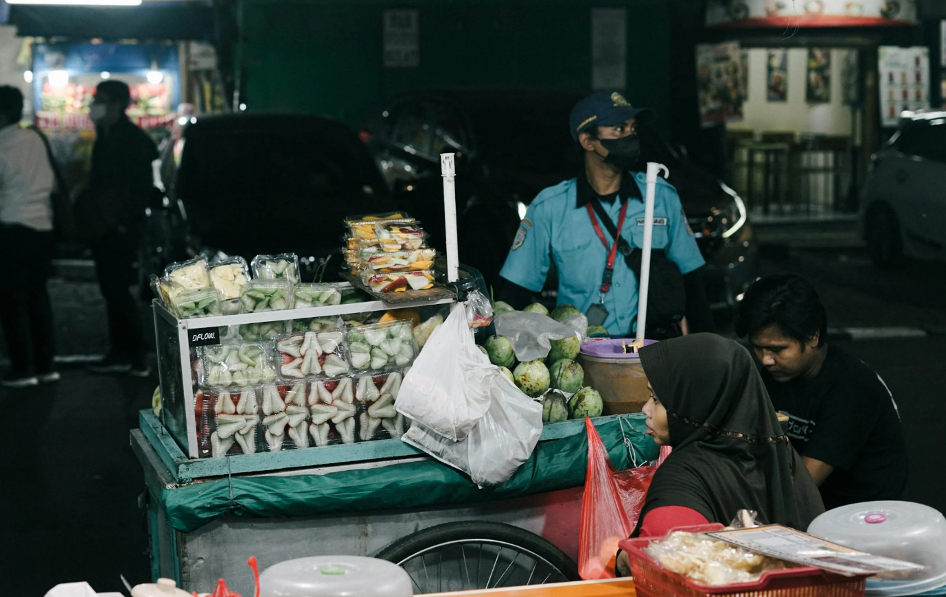 A person sitting at a fruit stand

Description automatically generated