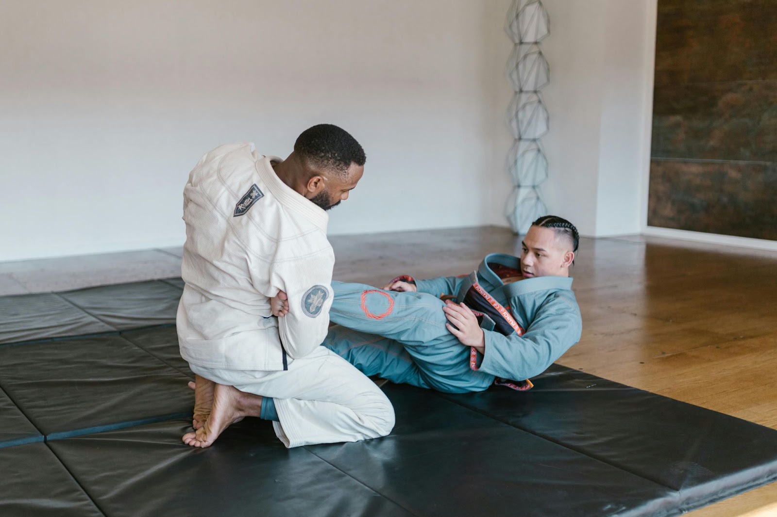 A martial arts instructor demonstrates a foot submission technique on a student lying on the ground.