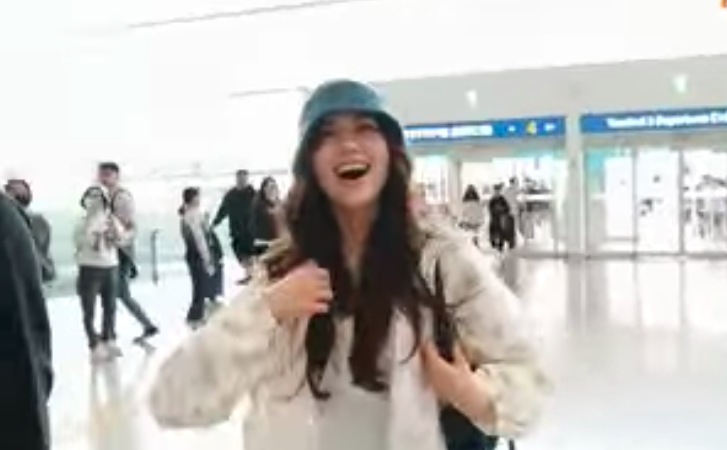 A picture of Olivia Marsh wearing a white jacket and a vest inside of it and a green cap at the airport